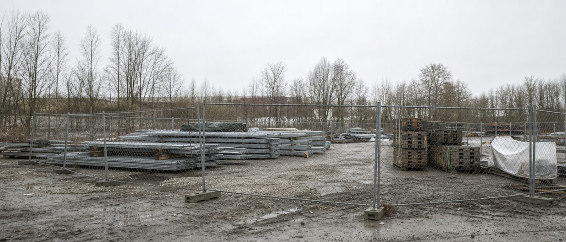 Eingezäunter Materiallagerplatz am Rand einer Baustelle bei Nacht